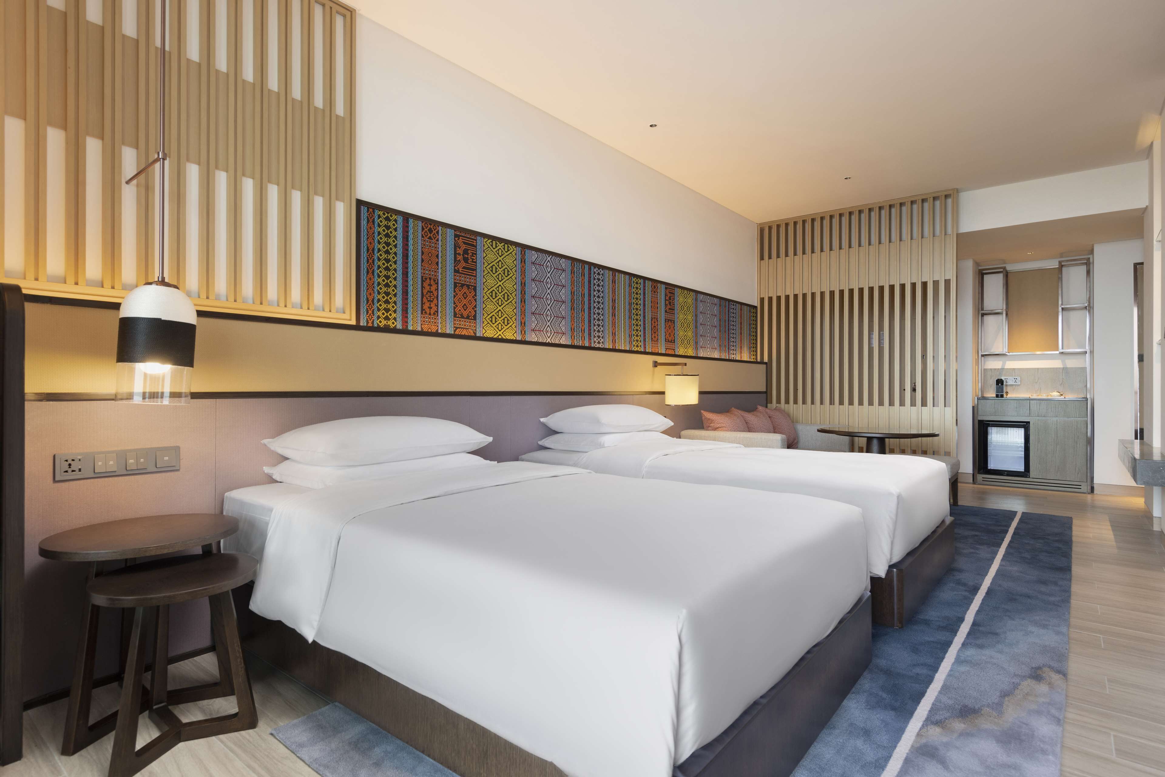 Een hotelkamer met twee bedden, een klein tafeltje, een stoel, een wandtelevisie en een kitchenette.