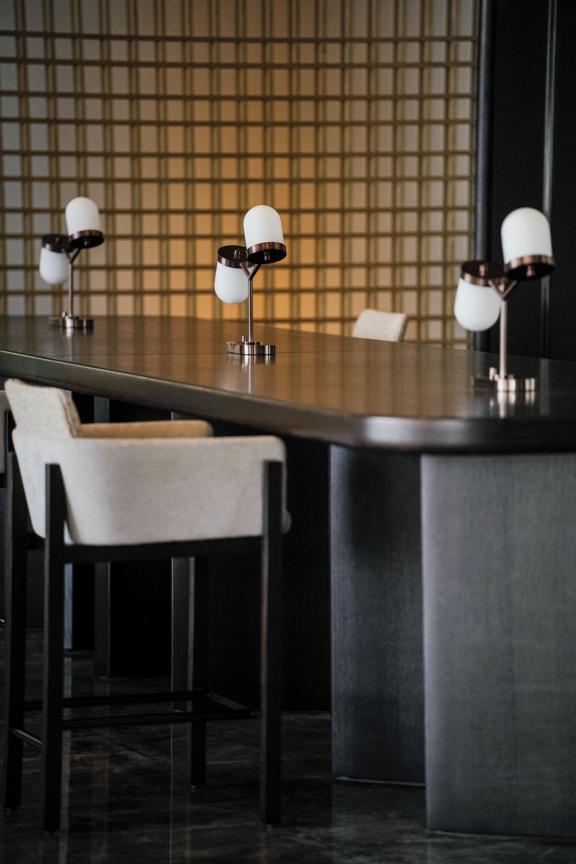 A modern bar area with a long counter, several chairs, and pendant lighting.