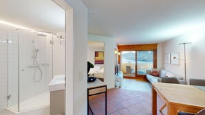 A modern bathroom with a glass-enclosed shower, a white sink, and a wooden table in the living area. - The newly renovated holiday apartment "Abitaziun Caspar Badrutt 306" in St. (St. Moritz)