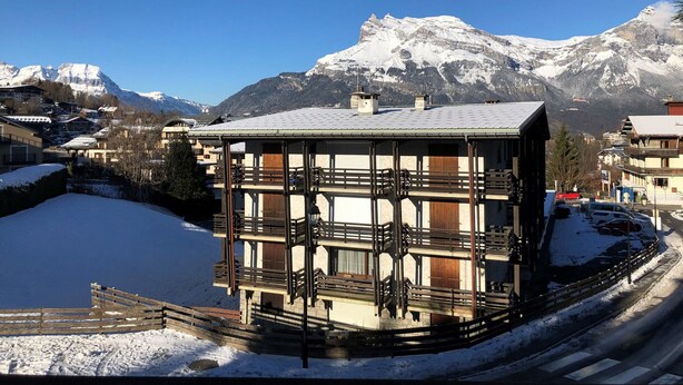 Un edificio de varios pisos con balcones, con montañas nevadas y un cielo azul claro al fondo.