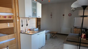 Cocina compacta con armarios de madera, un lavamanos y un pequeño comedor con una mesa dispuesta para dos personas.