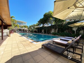 A poolside area with lounge chairs, a pool, and a building in the background. - Parkview Paradise – 2BR Bali Resort in Kingscliff (Tweed)