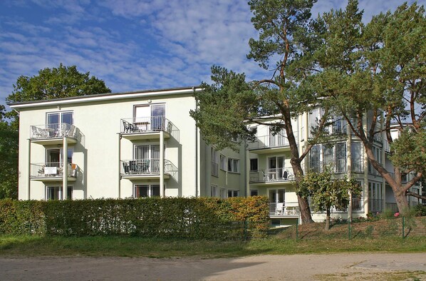 A multi-story residential building with balconies, a hedge in front, and trees nearby. - House Strandoase 22 - only a few meters to the beach (Heringsdorf (Seebad))