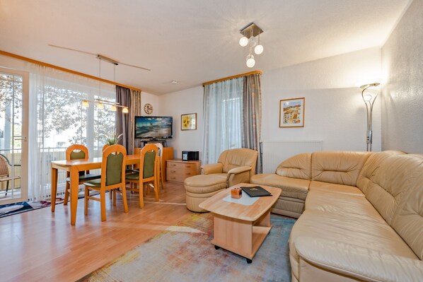 Ein modernes Wohnzimmer mit einer Couch, einem Esstisch mit Stühlen, einem Fernseher und einer Lampe.