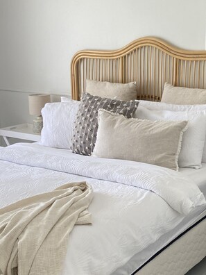 A neatly made bed with a wooden headboard, white bedding, and a bedside lamp. - Coastal family home central to everything! (Culburra Beach)