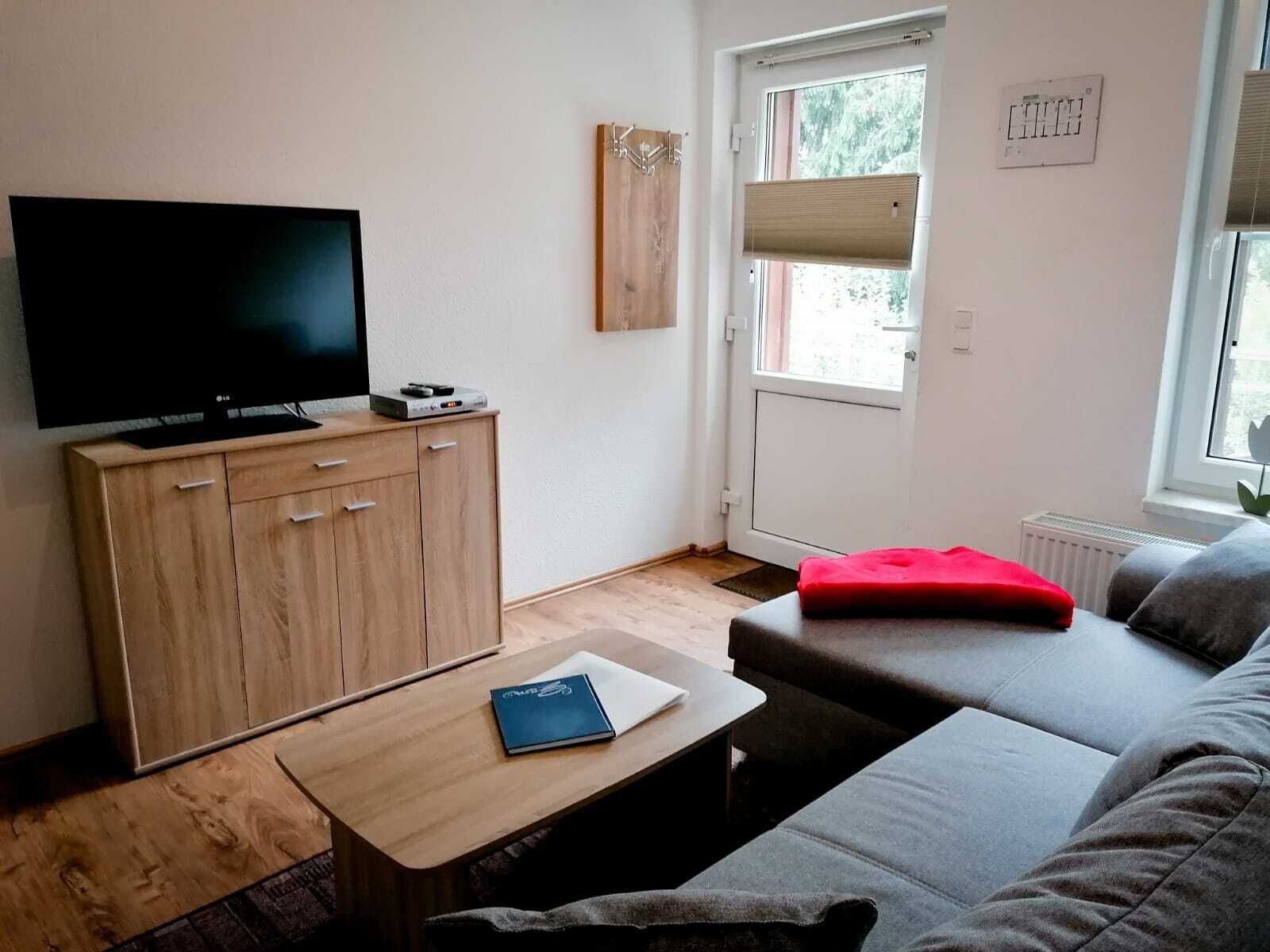 A modern living room with a flat-screen TV, wooden cabinet, and a grey sofa.