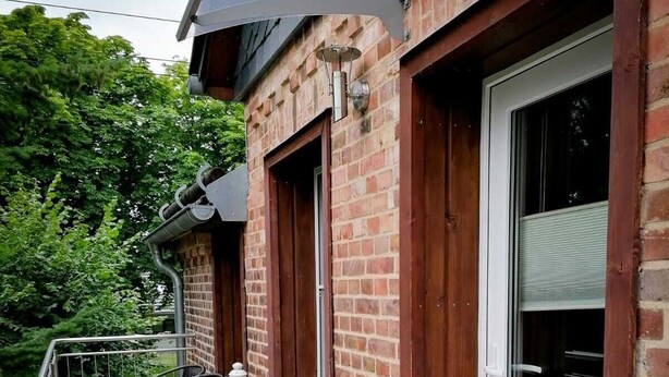 Een bakstenen gebouw met een balkon, terras en een deur met een raam.