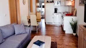 Een compacte woonruimte met een bank, een salontafel, een eethoek en een kitchenette.