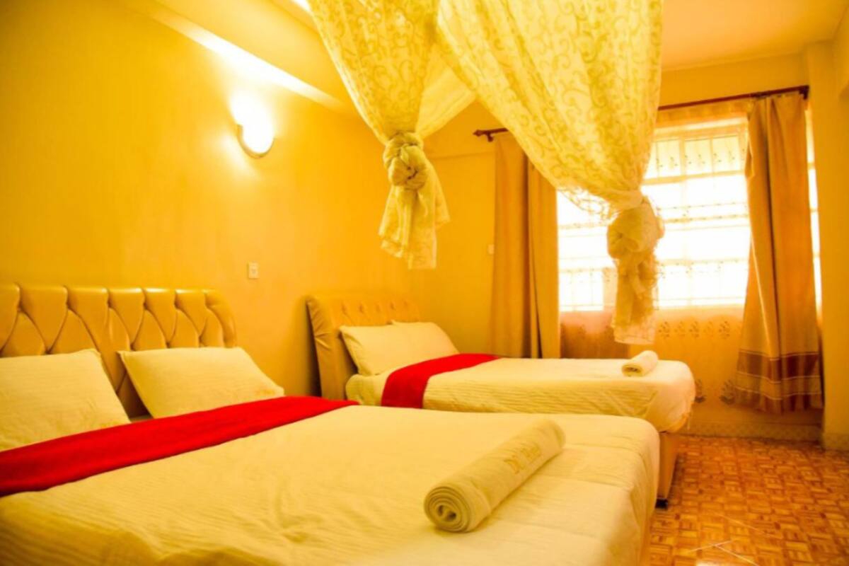 A hotel room with two beds, a red bedspread, a canopy bed, and a window with curtains.
