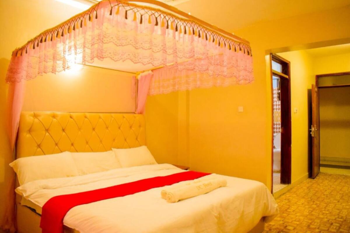 A hotel room with a large bed, a canopy, and a door leading to the bathroom.