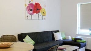 A living room with a dark grey sofa, a round wooden table, and a painting of flowers on the wall. - Vacation apartment Am Obstbaum "Apple" (Golßen OT Zützen)