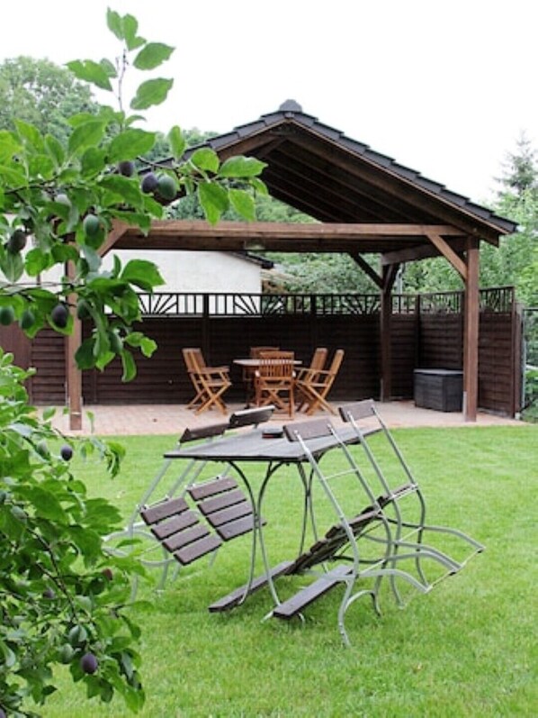 A covered patio area with a table and chairs, surrounded by a wooden fence and greenery. - Vacation apartment Am Obstbaum "Apple" (Golßen OT Zützen)