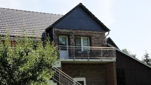 A two-story building with a brick facade, a balcony on the upper floor, and a staircase leading to the entrance. - Ferienwohnung "birne" Am Obstbaum (Golßen OT Zützen)