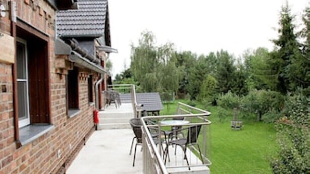 A brick building with a balcony, outdoor seating, and a garden. - Ferienwohnung "birne" Am Obstbaum (Golßen OT Zützen)