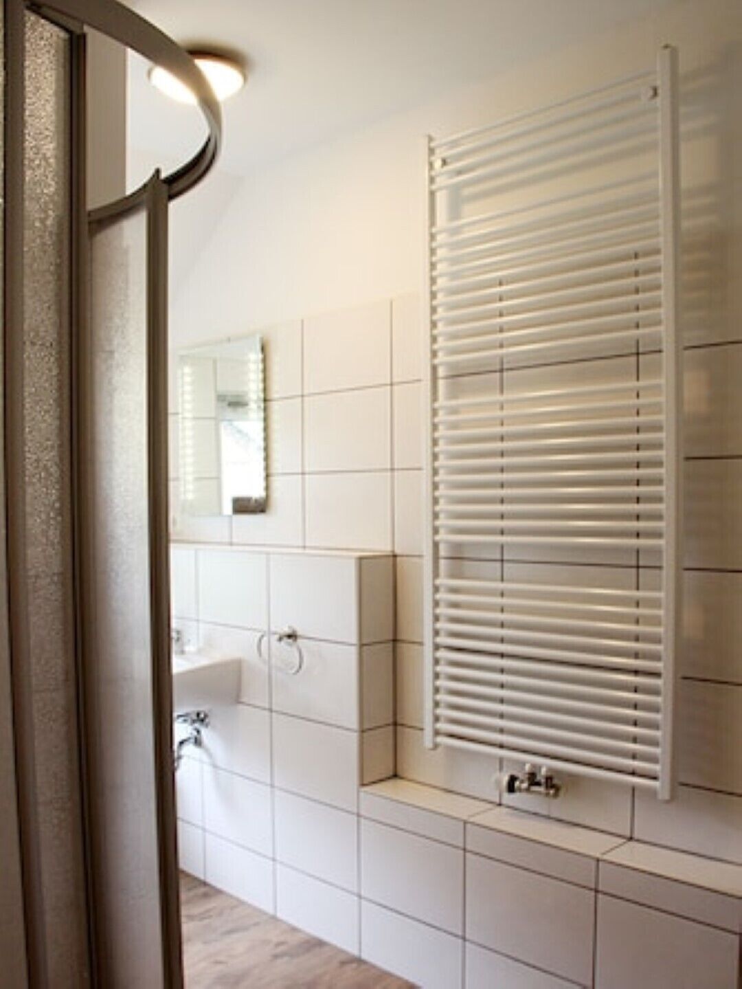 Un baño con pared de azulejos blancos, un lavamanos, un espejo y un perchero para toallas.