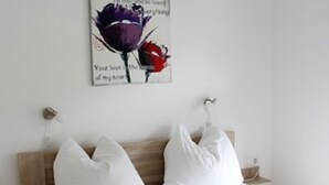 A neatly made bed with white linens and pillows, a wooden headboard, and a wall-mounted artwork of purple and red flowers with text. - Ferienwohnung "birne" Am Obstbaum (Golßen OT Zützen)