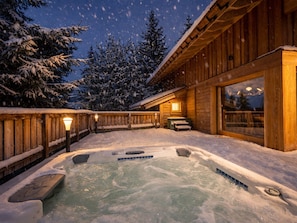 Une cabane en bois avec un bain à remous, entourée d’arbres couverts de neige.