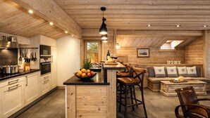 A modern kitchen with wooden accents, a central island, and a cozy seating area with a sofa and chairs. - Luxurious Chalet in Courchevel-La Tania: Sleeps 12, Ski-in/Ski-out, Jacuzzi, Sauna & Home Cinema (La Tania)