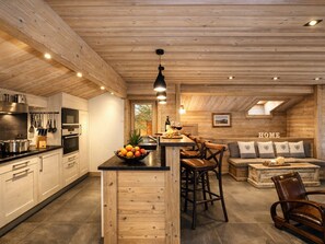 Uma cozinha moderna com detalhes em madeira, uma ilha central e um espaço de estar acolhedor com sofá e cadeiras.