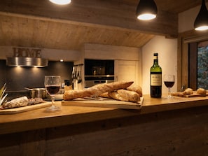Un comptoir de cuisine en bois avec du pain, des verres à vin et une bouteille de vin.