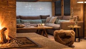 A cozy living room with a stone fireplace, a sofa, and a unique wooden sculpture. - Luxurious Chalet in Courchevel-La Tania: Sleeps 12, Ski-in/Ski-out, Jacuzzi, Sauna & Home Cinema (La Tania)