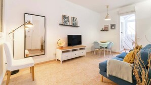 Un salon avec un téléviseur, un canapé blanc, une table à manger avec des chaises et un grand miroir.