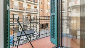 Un balcon doté d’une rambarde en métal, d’une chaise noire et offrant une vue sur une rue bordée de voitures garées et d’immeubles.