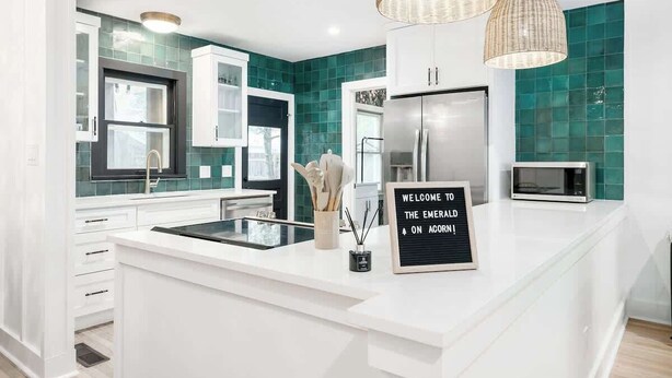 A modern kitchen with white cabinetry, a central island, a stainless steel refrigerator, and teal backsplash tiles.