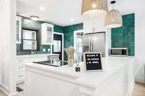 Une cuisine moderne avec des meubles blancs, un îlot central, un four à micro-ondes et un panneau indiquant : « Bienvenue à nos invités ».