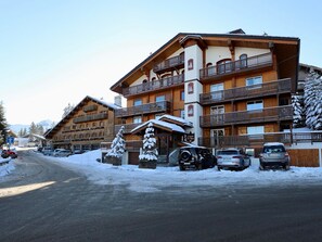 Ein mehrstöckiges Holzhotel mit Balkonen, einem verschneiten Eingang und geparkten Autos.