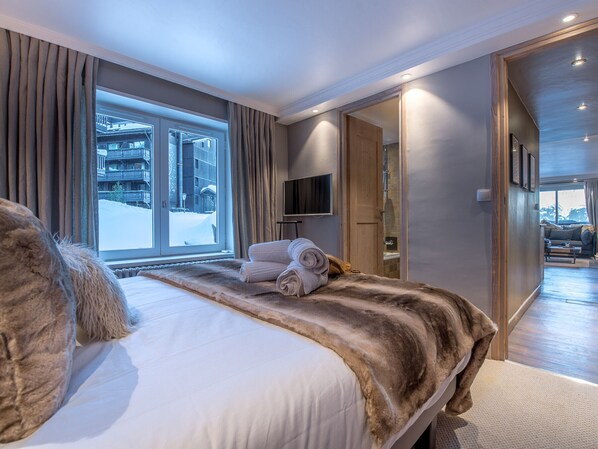 Ein modernes Hotelzimmer mit einem großen Bett, einem Flachbildfernseher und Blick auf eine verschneite Landschaft.
