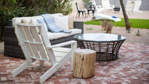 Un patio amueblado con un sofá de mimbre blanco, una mesa redonda de cristal y un taburete de madera.