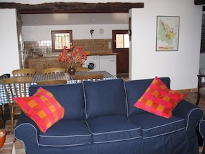 Una sala de estar con un sofá azul, una mesa de comedor con sillas, una cocina al fondo y un mapa en la pared.