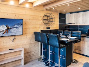 A modern interior with a wooden wall, a bar area with black leather chairs, and a ski-themed painting. - Renovated mountain apartment, 6 people, near slopes and amenities (Val Thorens)
