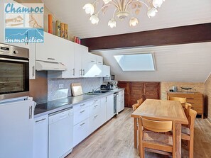Een moderne keuken met witte kasten, een inbouwoven en een eethoek met een houten tafel en stoelen.