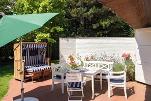 An outdoor patio with a dining table, chairs, a striped lounge chair, and a green umbrella.