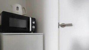 Una cocina compacta con microondas y tetera sobre un mueble blanco.