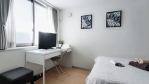 Una habitación de hotel moderna con un escritorio blanco, una silla negra, una cama con cubierta blanca y dos cuadros con motivos florales en la pared.
