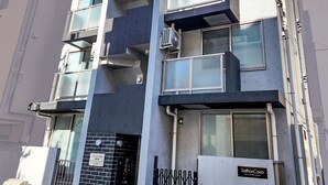 Un edificio moderno de varios pisos con balcones, unidades de aire acondicionado y una entrada con portón.