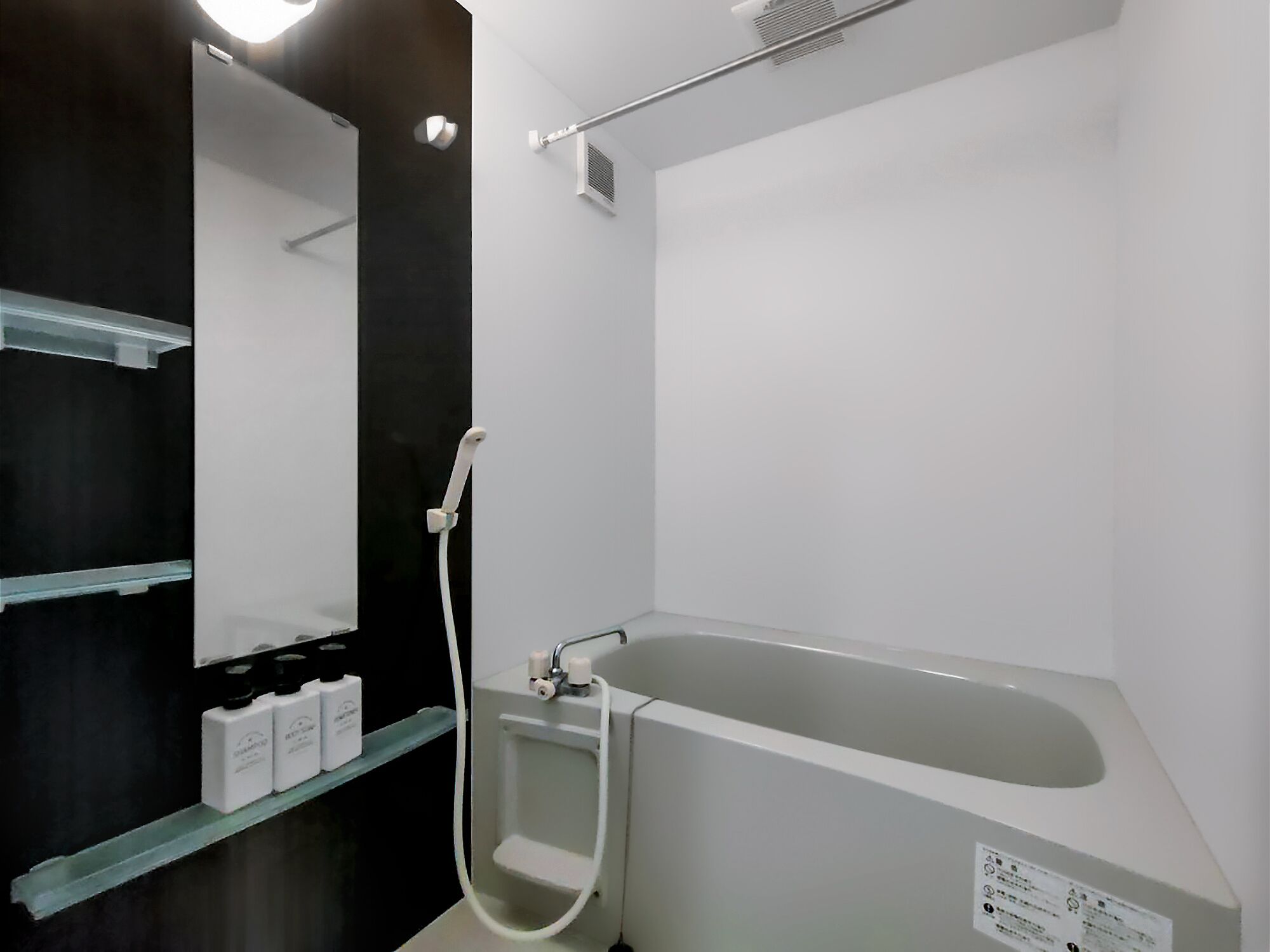 A modern bathroom with a large bathtub, a glass shelf with toiletries, and a mirror.