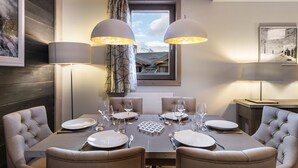 A dining room with a table set for four, two pendant lights, a window with a view, and a framed picture on the wall. - Modern apartment in Courchevel with parking and WiFi (Courchevel 1550)