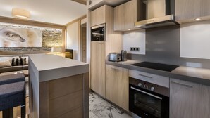 A modern kitchen with a central island, built-in appliances, and a stone accent wall. - Modern apartment in Courchevel with parking and WiFi (Courchevel 1550)