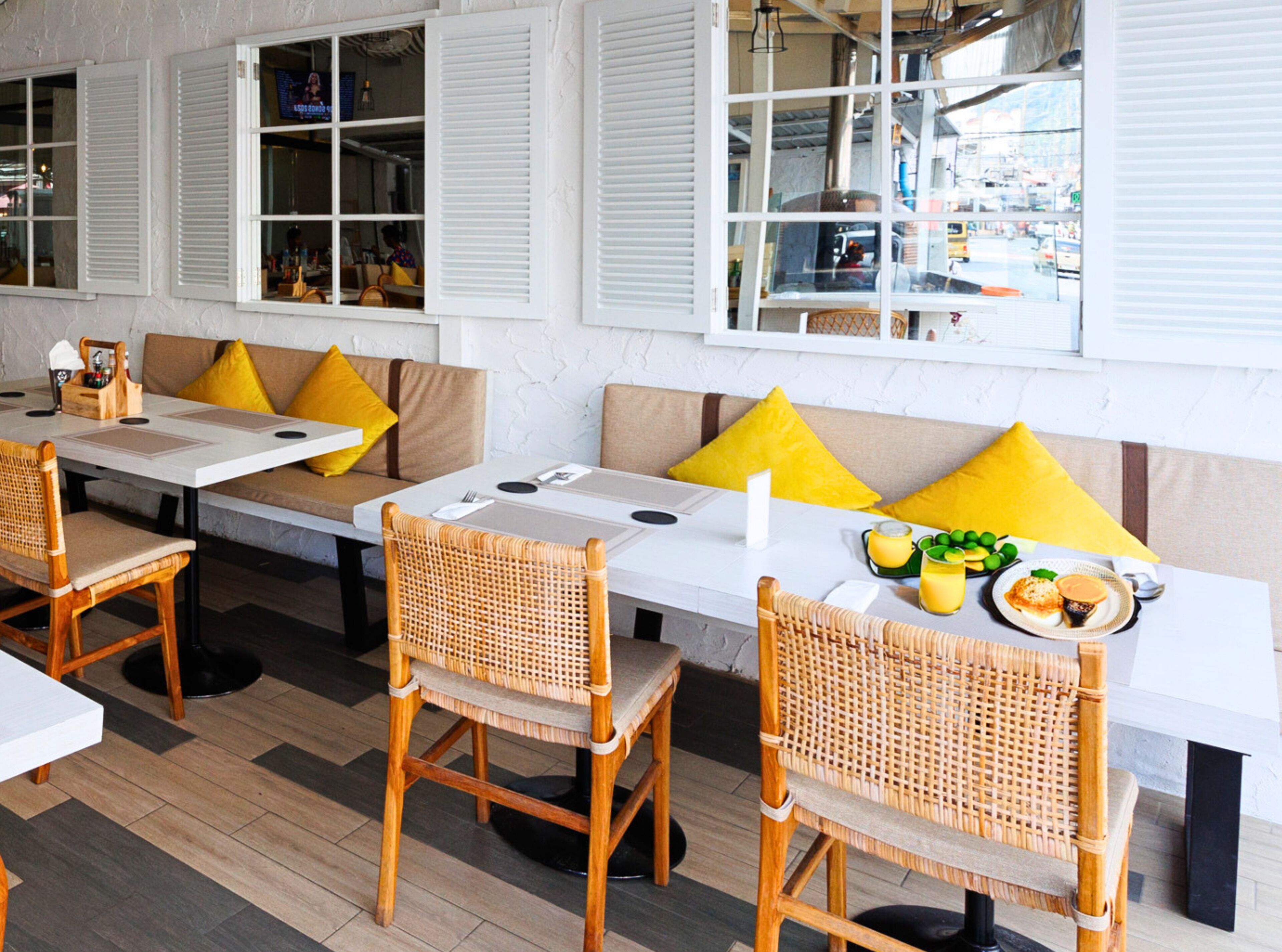 A restaurant with outdoor seating, white tables, and wicker chairs.