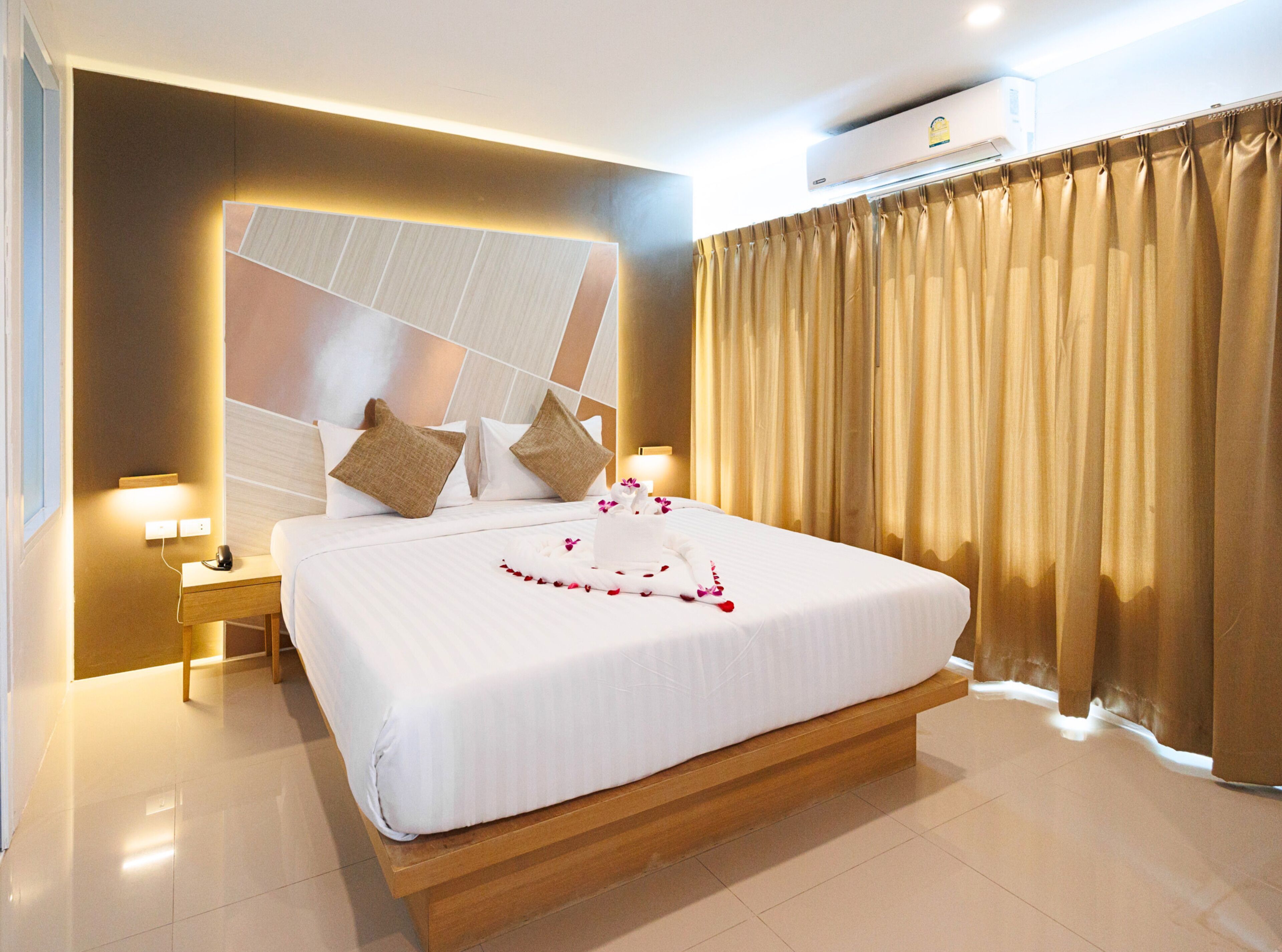 Habitación de hotel con una cama grande, un cabecero de madera, una mesita de noche con lámpara y una ventana con cortinas.