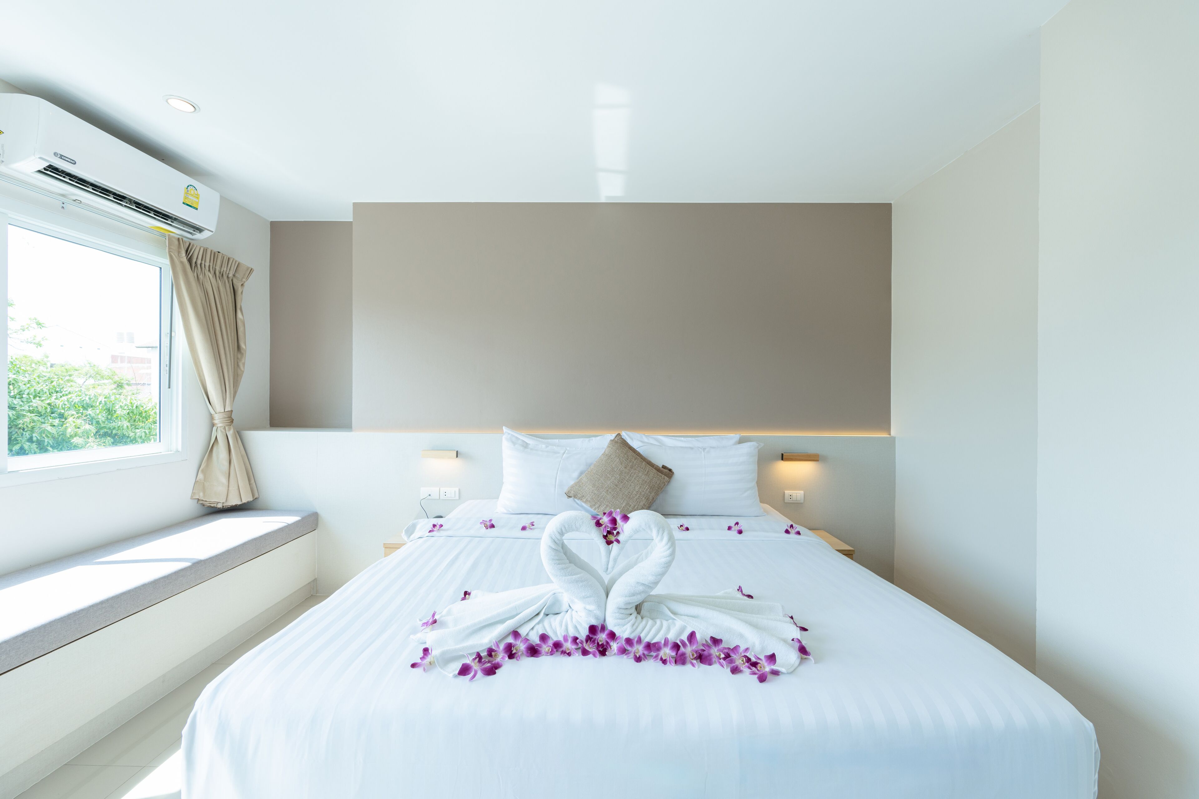 Una habitación de hotel con una cama grande, una ventana con cortinas, un aire acondicionado de pared y una mesita de noche con lámpara.