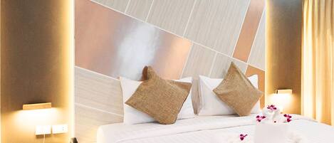 A hotel room with a large bed, two pillows, a bedside table with a lamp, and a wall with a geometric pattern.
