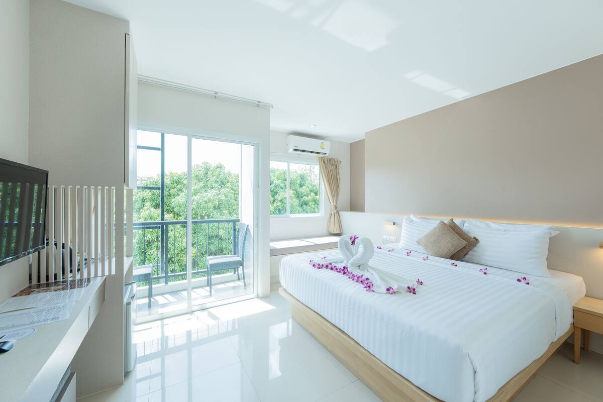Een moderne hotelkamer met een groot bed, een televisie, een balkon met een stoel en uitzicht op groen.