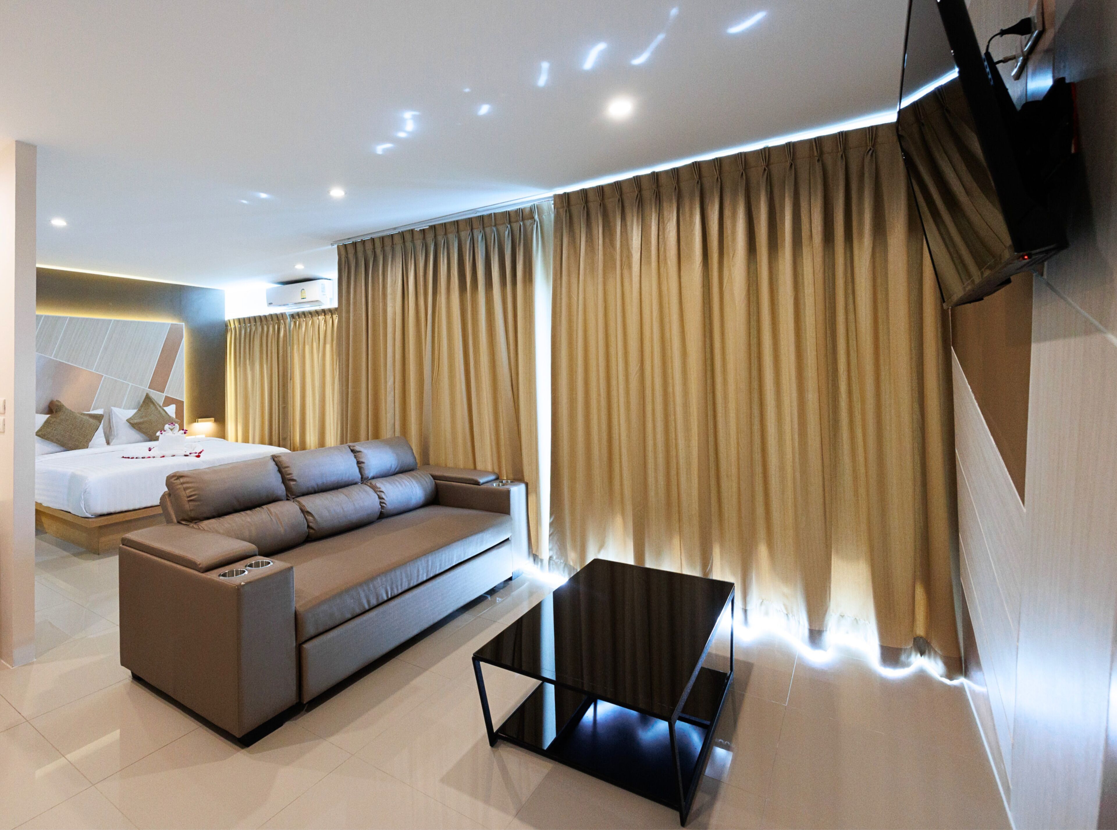 Une chambre d’hôtel moderne, dotée d’un grand lit, d’un canapé, d’une table basse et d’un téléviseur fixé au mur.