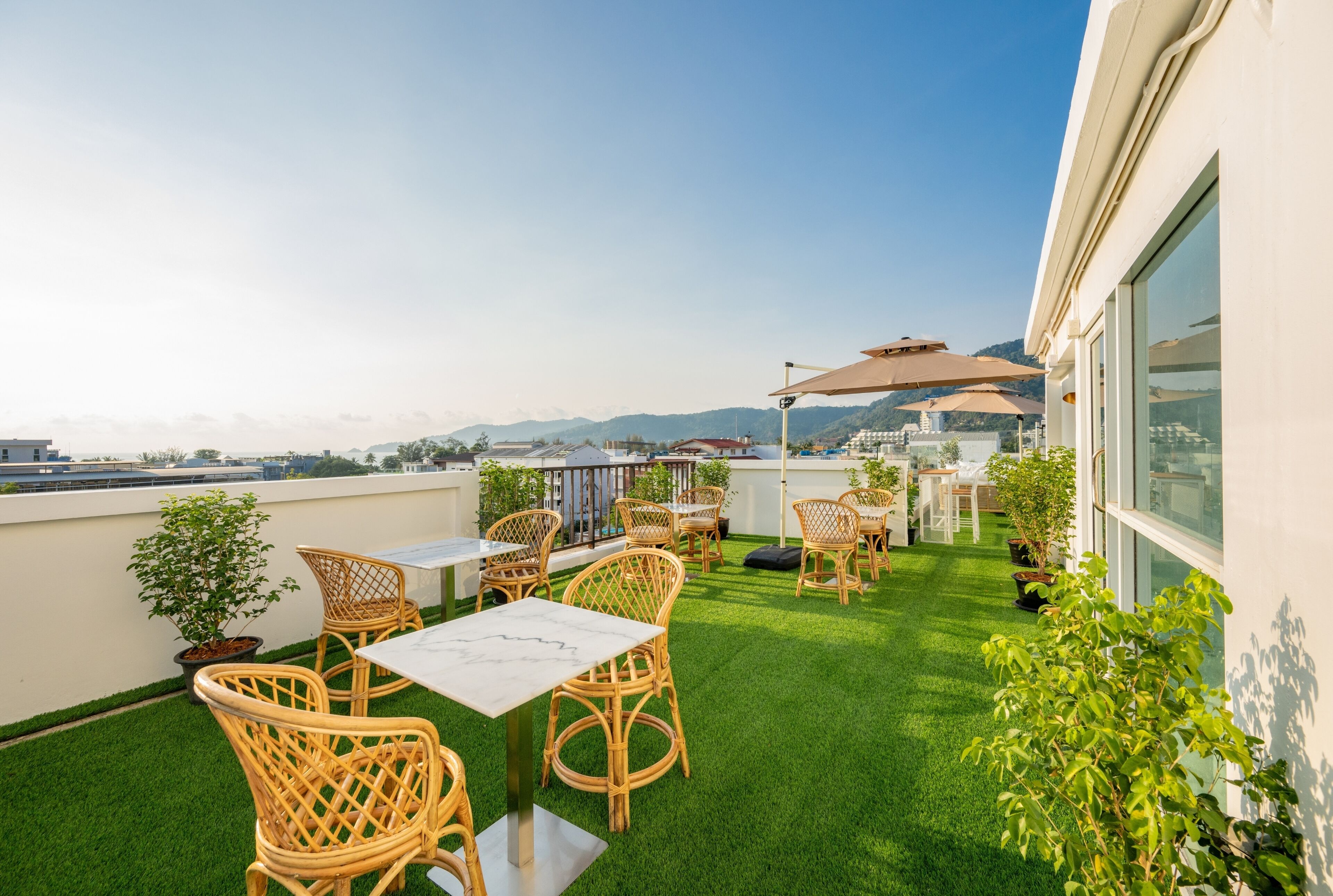 A rooftop terrace with wicker furniture, a table, and potted plants.