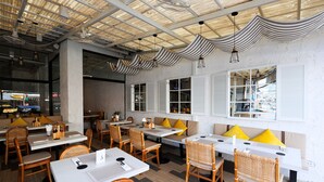 Un restaurante con techos altos, tela a rayas colgando del techo y una mezcla de muebles de madera y mimbre.